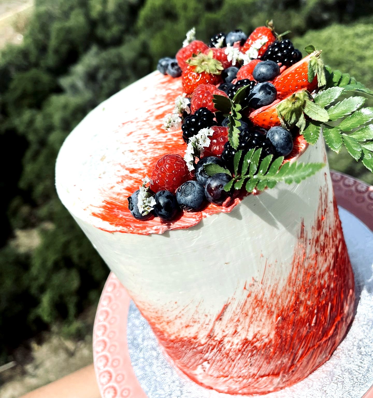 Tarta blanca con pinceladas rojas, frutos rojos, arandanos y hojas verdes.