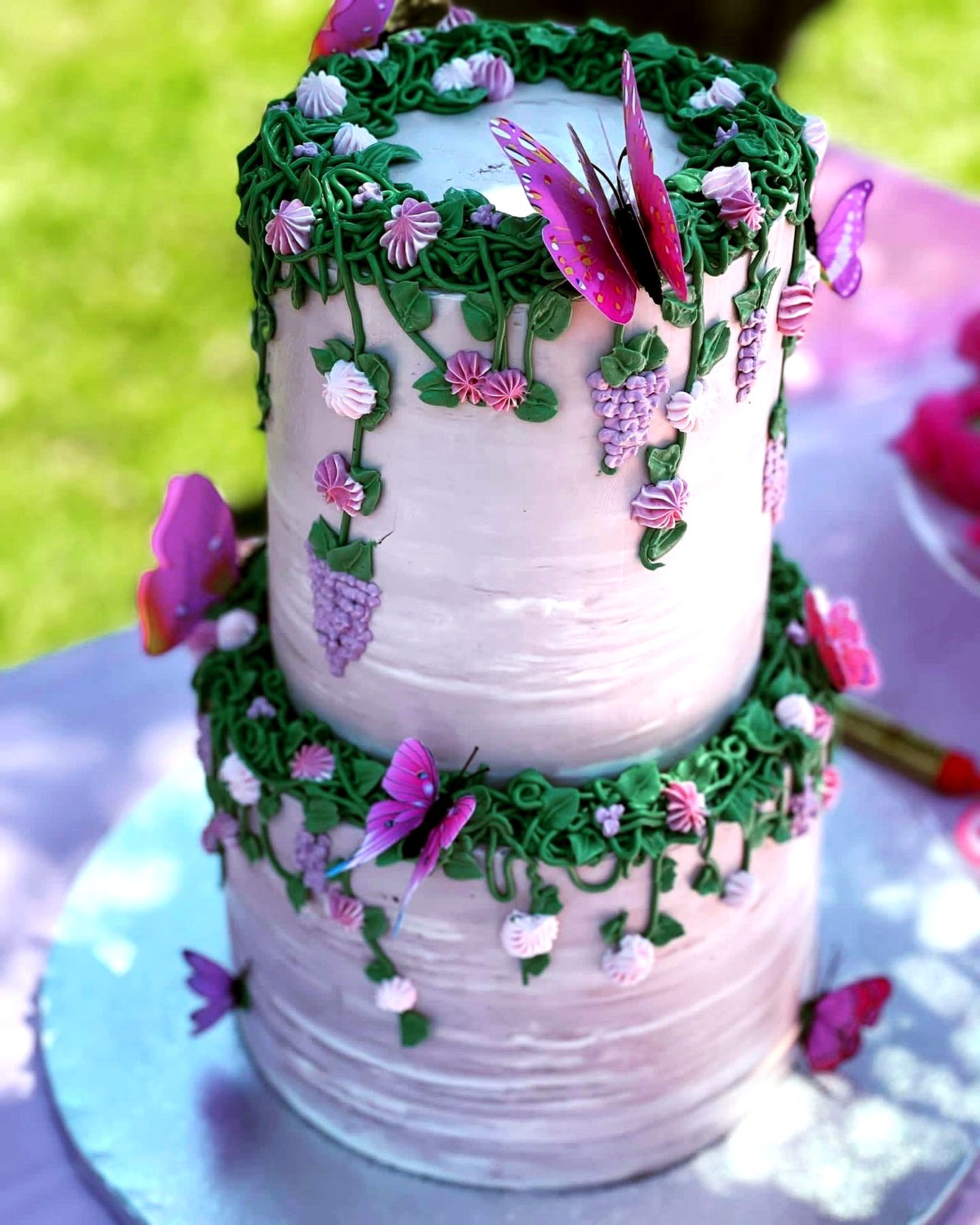 Tarta rosa con enredaderas verdes, flores pequenas y mariposas moradas.