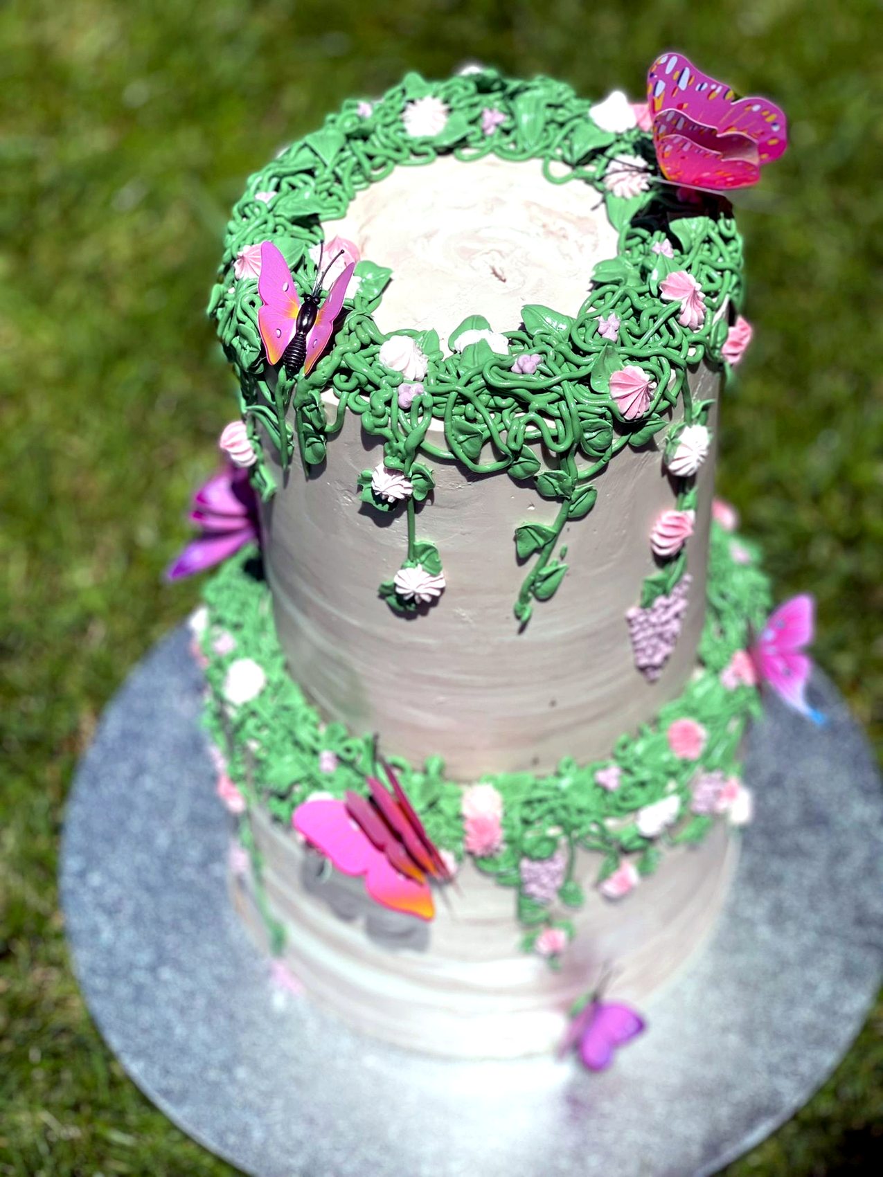 Tarta alta rosa con enredaderas verdes y mariposas en primer plano.