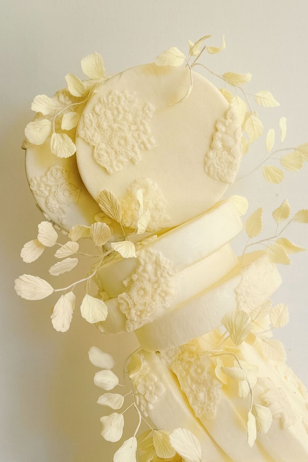 Tarta blanca de dos niveles con flores y hojas delicadas en tonos marfil.