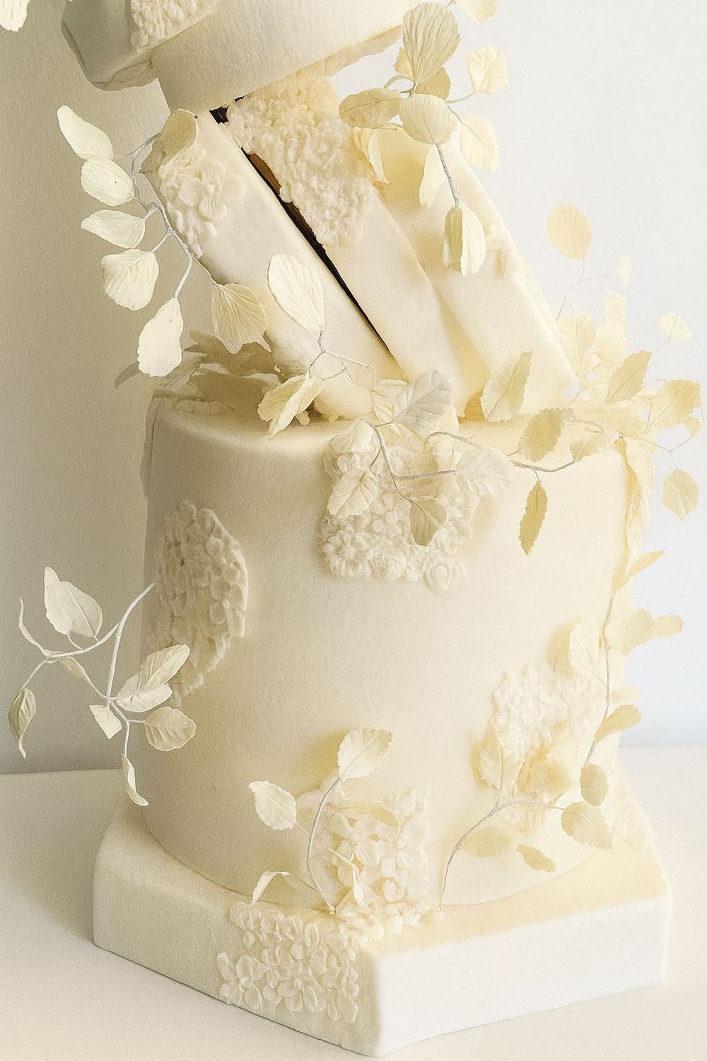 Tarta blanca de celebracion con acabado geometrico, flores claras y ramas decorativas.