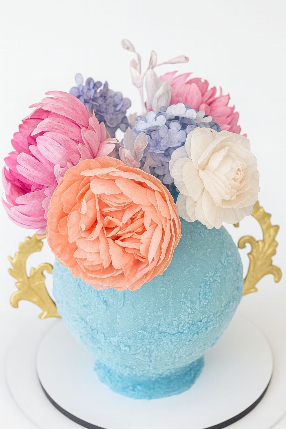 Tarta azul con forma de tetera, asas doradas y flores grandes en rosa, melocoton y lila.