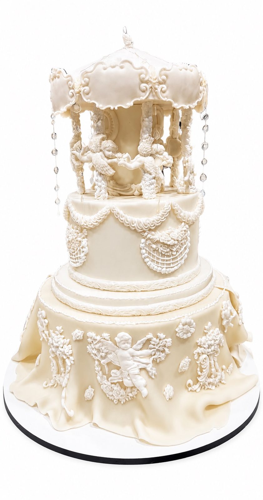 Tarta alta color marfil con carrusel, querubines, guirnaldas y detalles ornamentales en relieve.