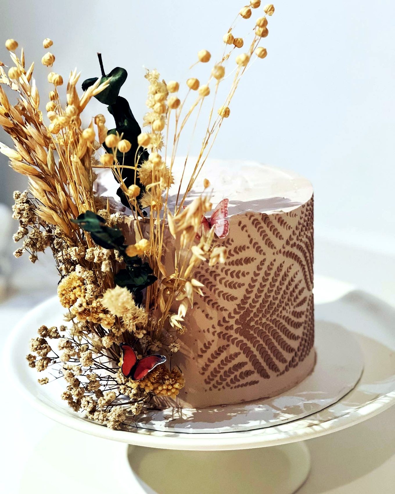 Tarta beige con flores secas, mariposas y patron lateral en tonos naturales.