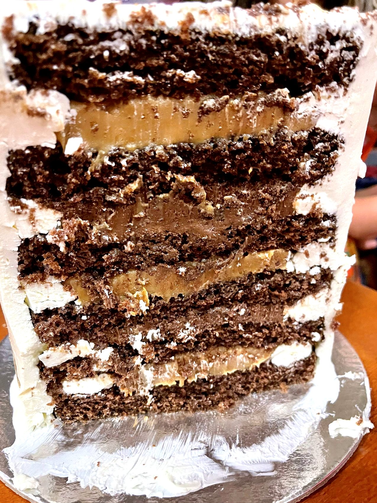 Corte de tarta de chocolate con capas de bizcocho, crema clara y rellenos caramelizados.