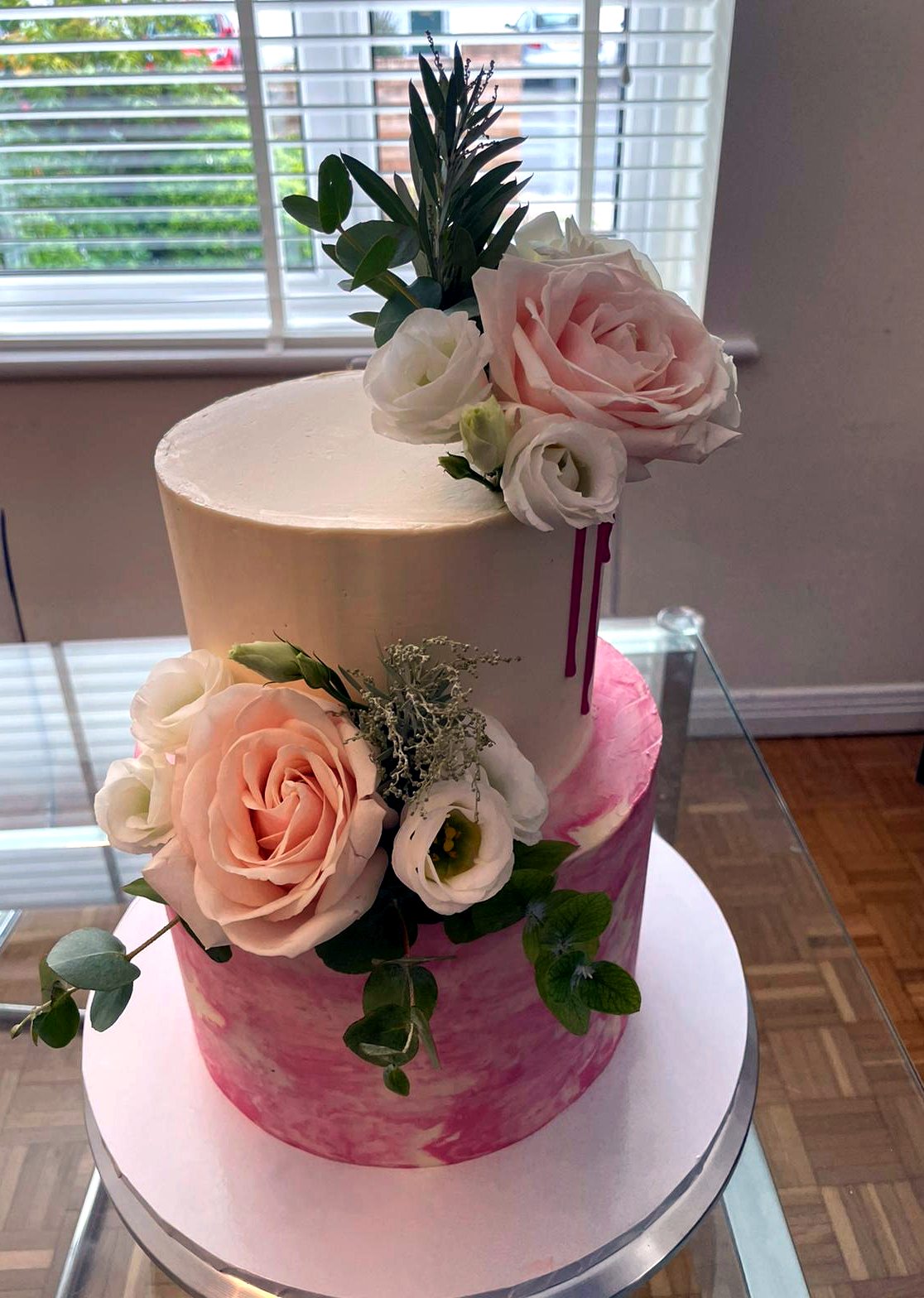 Tarta de dos niveles con marmolado rosa, crema clara, rosas y follaje natural.