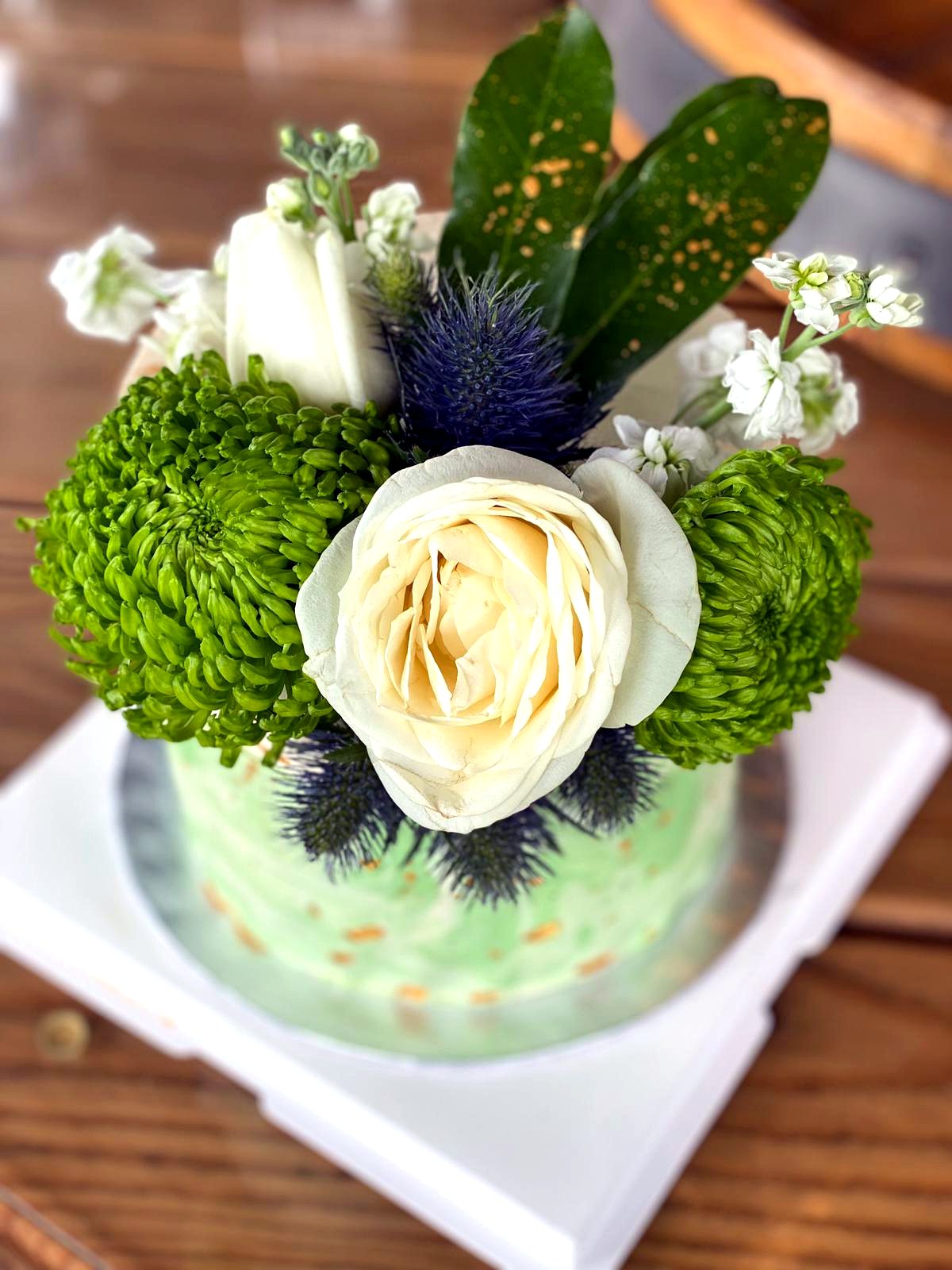 Vista superior de tarta con flores verdes y blancas frescas sobre crema clara.