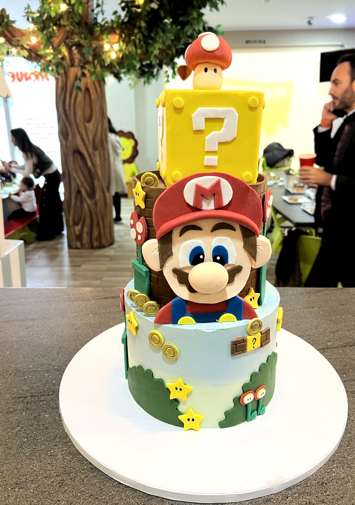 Tarta de Mario con cubo amarillo, base blanca, monedas y detalles de juego.