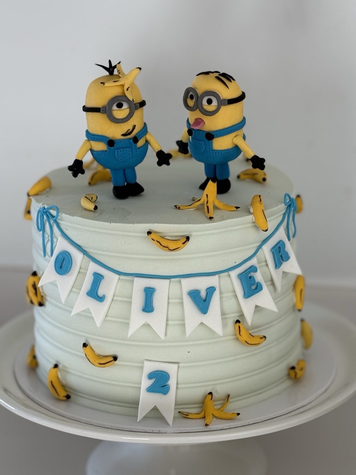 Tarta de cumpleanos con dos figuras amarillas, banderines con nombre y detalles azules.