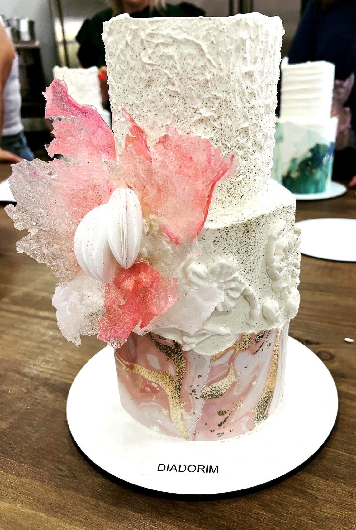 Tarta alta con marmolado rosa, detalles dorados y flores de azucar translucidas.