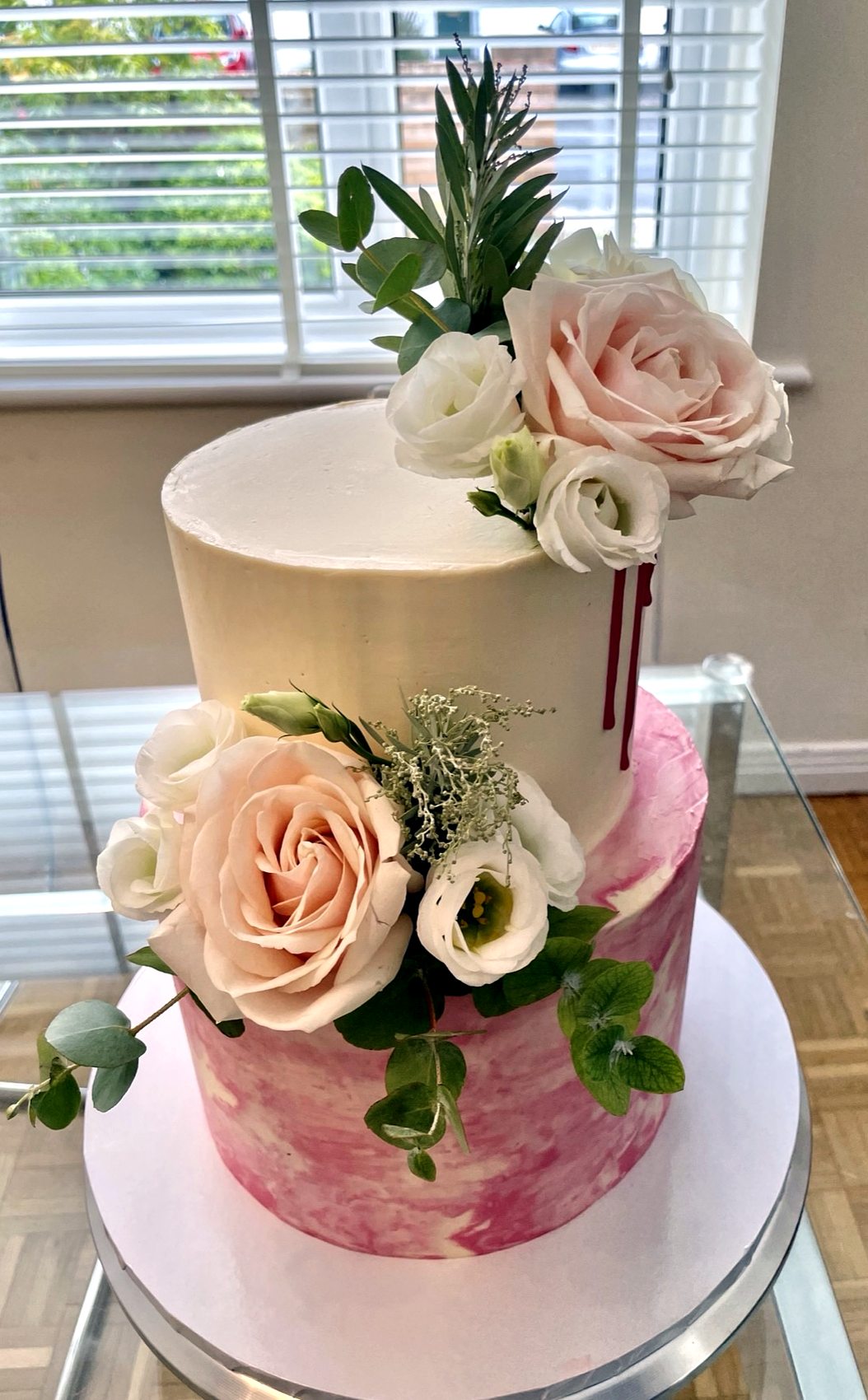 Tarta floral de dos niveles con rosas claras y verdes sobre base rosa marmolada.