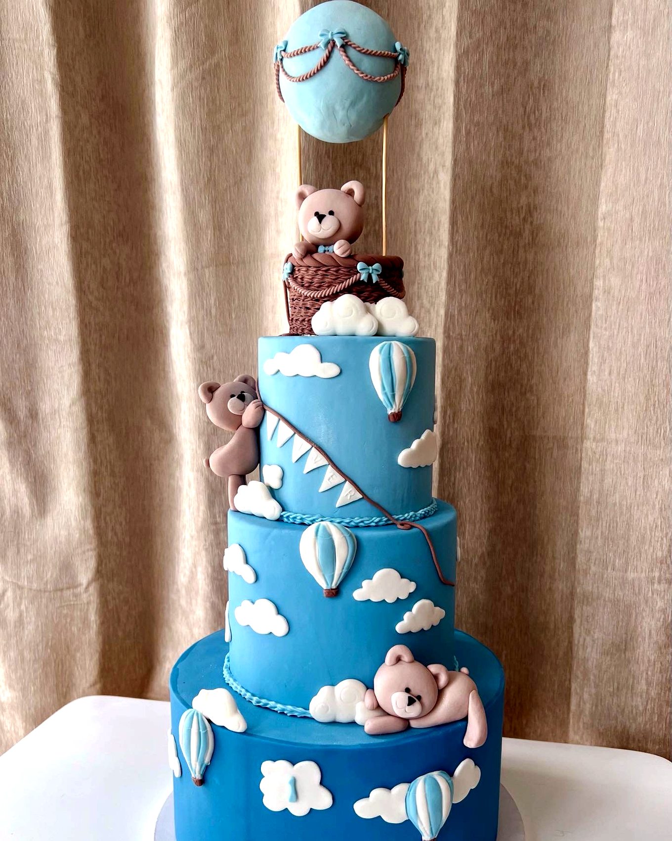 Tarta azul de varios niveles con ositos, globos aerostaticos y nubes blancas.