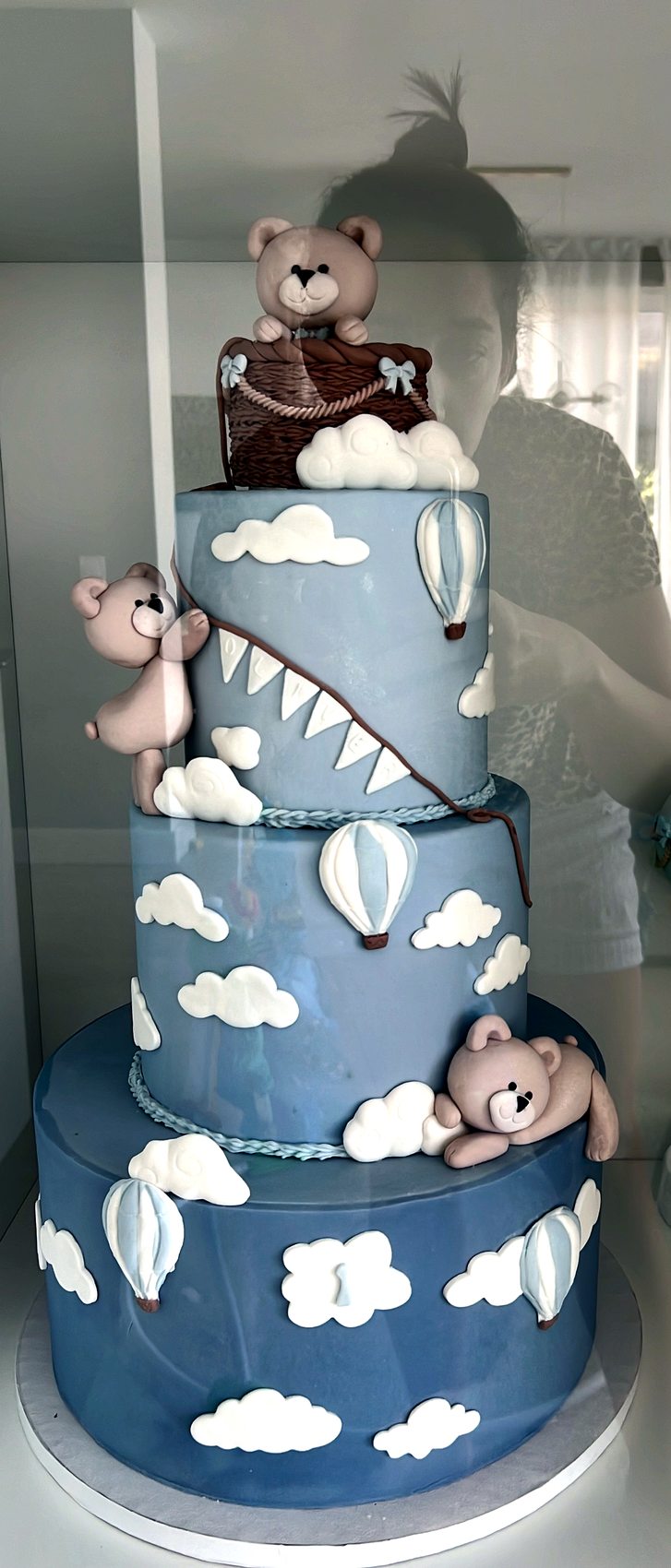 Tarta azul con ositos, nubes y globos fotografiada en vitrina.